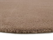 Nahaufnahme eines runden, beigen Teppichs mit weicher, flauschiger Textur, seitliche Perspektive.