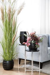 Schwarze Keramikvase COCON in modernem Wohnzimmer, frontal auf einem silbernen Beistelltisch präsentiert, umgeben von dekorativen Pflanzen.