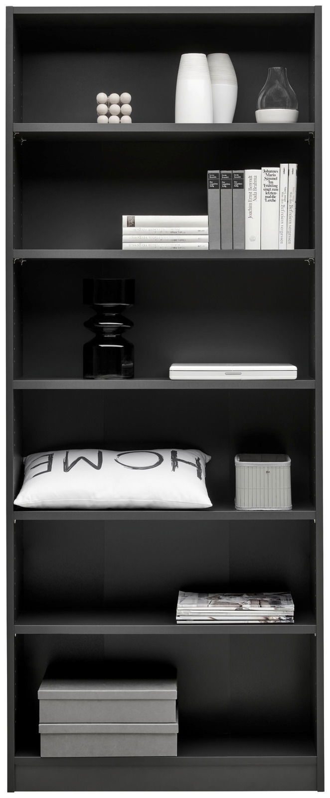 Schwarzes Regal mit mehreren Fächern, gefüllt mit Büchern, Dekorationsgegenständen und Kissen, frontal fotografiert.