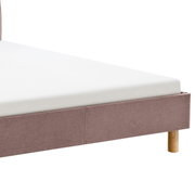 Close-up van een gestoffeerd bed met een lichtbruine stoffen bekleding en houten poten, gezien vanaf de zijkant.