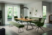 Moderner Esstisch aus Holz mit Metallbeinen, umgeben von grünen Polsterstühlen und einer Bank, in einem hellen Wohnzimmer mit Blick auf den Garten.