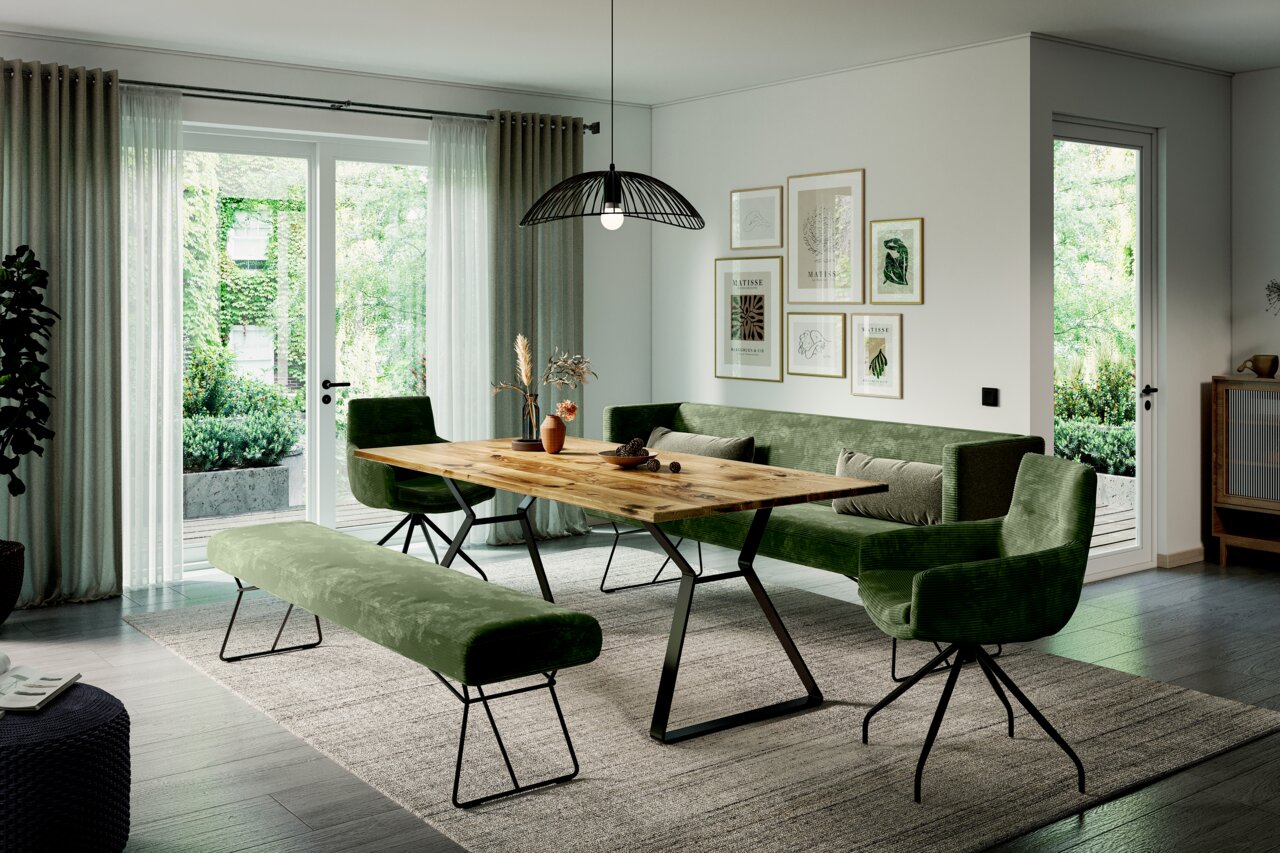 Een moderne houten eettafel met metalen poten, omringd door groene gestoffeerde stoelen en een bank, in een lichte woonkamer met uitzicht op de tuin.