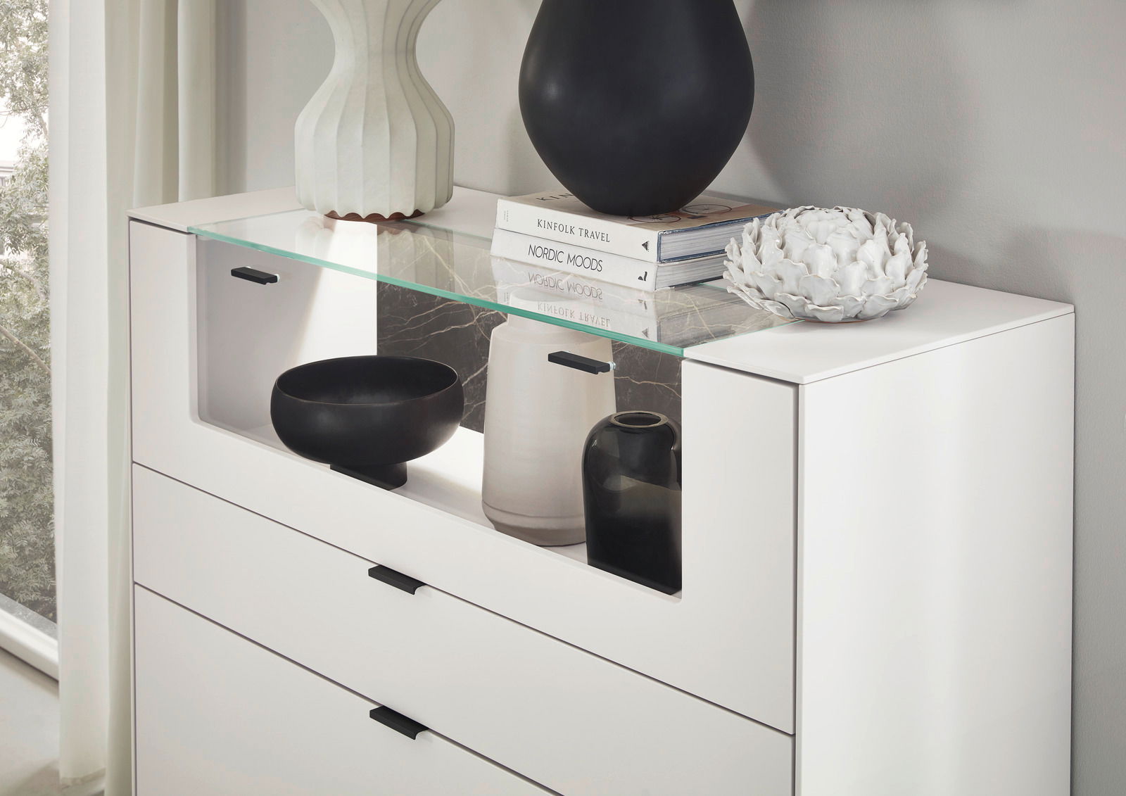 Weißes Highboard mit Glasablage, dekoriert mit Vasen und Büchern, seitliche Perspektive