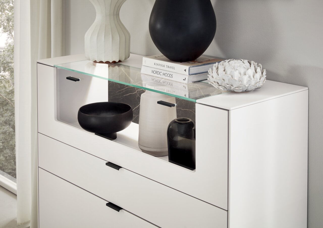 Weißes Highboard mit Glasablage, dekoriert mit Vasen und Büchern, seitliche Perspektive