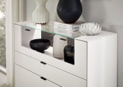 Weißes Highboard mit Glasablage, dekoriert mit Vasen und Büchern, seitliche Perspektive