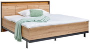 Holzbett mit Kopfteil, weißer Bettwäsche und grüner Decke, seitliche Perspektive
