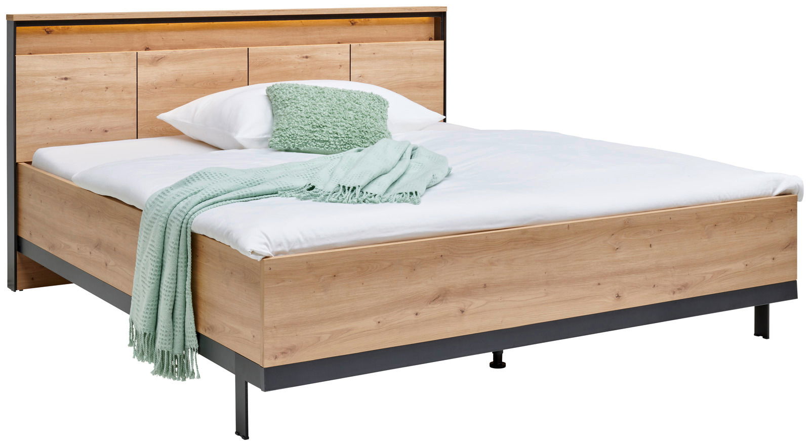 Holzbett mit Kopfteil, weißer Bettwäsche und grüner Decke, seitliche Perspektive