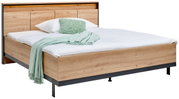 Holzbett mit Kopfteil, weißer Bettwäsche und grüner Decke, seitliche Perspektive