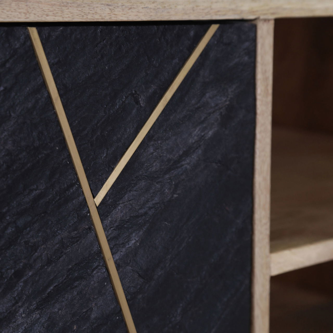 Nahaufnahme eines TV-Lowboards mit schwarzer Steinoptik und goldenen Zierleisten, seitliche Perspektive.