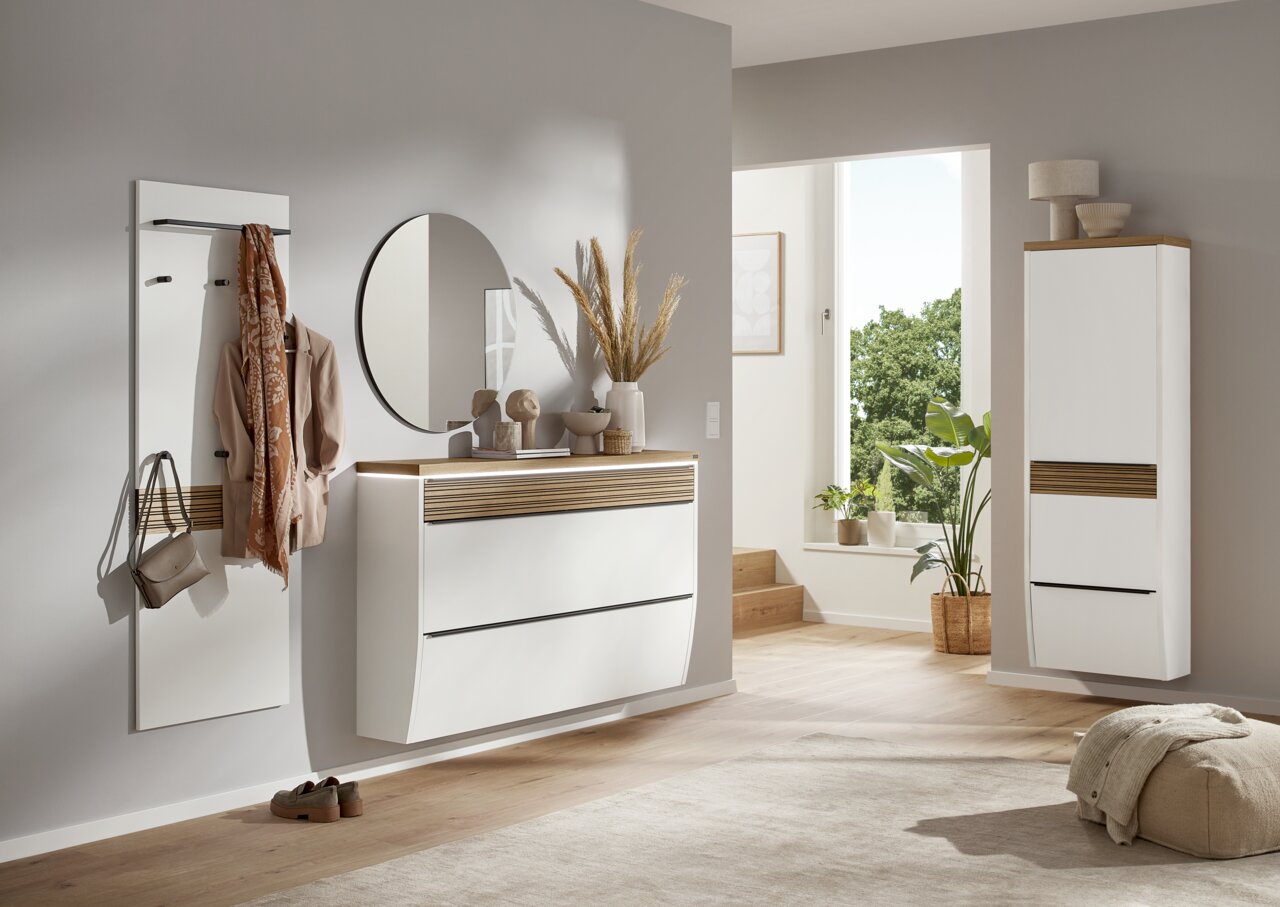 Dieter Knoll XXL-Hängeschuhschrank ARCO NOVA Moderner Eingangsbereich mit weißem Hängeschuhschrank, rundem Spiegel und Garderobenpaneel, seitliche Perspektive.