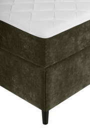 Ecke eines Boxbetts mit dunkelgrünem Stoffbezug und schwarzem Bein, aus der Perspektive von unten links fotografiert.