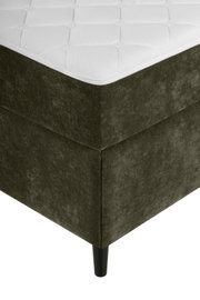 Ecke eines Boxbetts mit dunkelgrünem Stoffbezug und schwarzem Bein, aus der Perspektive von unten links fotografiert.