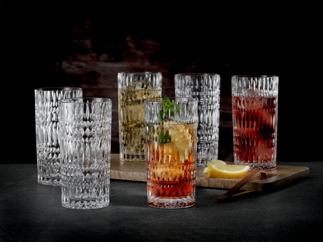 Nachtmann Longdrinkglas ETHNO Sechs Longdrinkgläser mit Ethno-Muster, gefüllt mit verschiedenen Getränken, auf einem dunklen Hintergrund. Perspektive von vorne.
