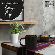 Schwarze Tasse aus dem Tassenset Nordic auf einem Tisch mit Deko-Pflanze und Schale, seitliche Perspektive.