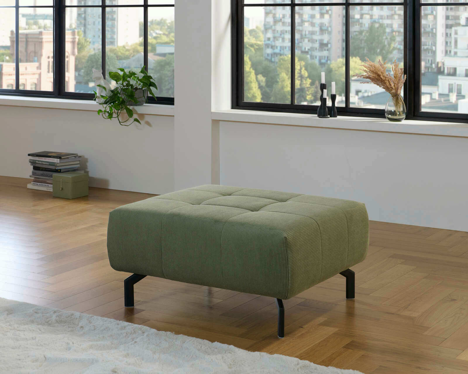 Grüner XL-Hocker in einem modernen Wohnzimmer mit Holzfußboden, seitliche Perspektive.