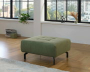 Grüner XL-Hocker in einem modernen Wohnzimmer mit Holzfußboden, seitliche Perspektive.