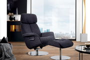 Moderner Relaxsessel mit Hocker in dunklem Stoffbezug, seitliche Perspektive, vor einem großen Fenster mit Stadtblick.