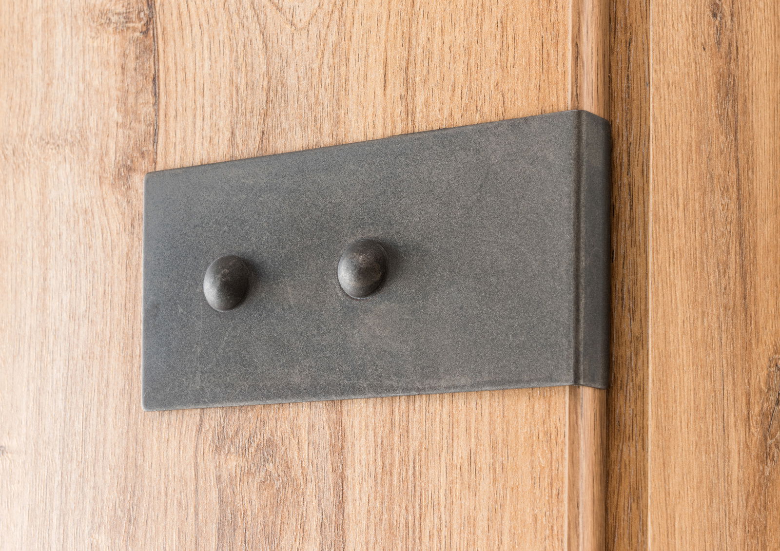 Nahaufnahme eines Holzschranks mit einer dunklen Metallplatte und zwei runden Knöpfen, seitliche Perspektive.