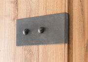 Nahaufnahme eines Holzschranks mit einer dunklen Metallplatte und zwei runden Knöpfen, seitliche Perspektive.