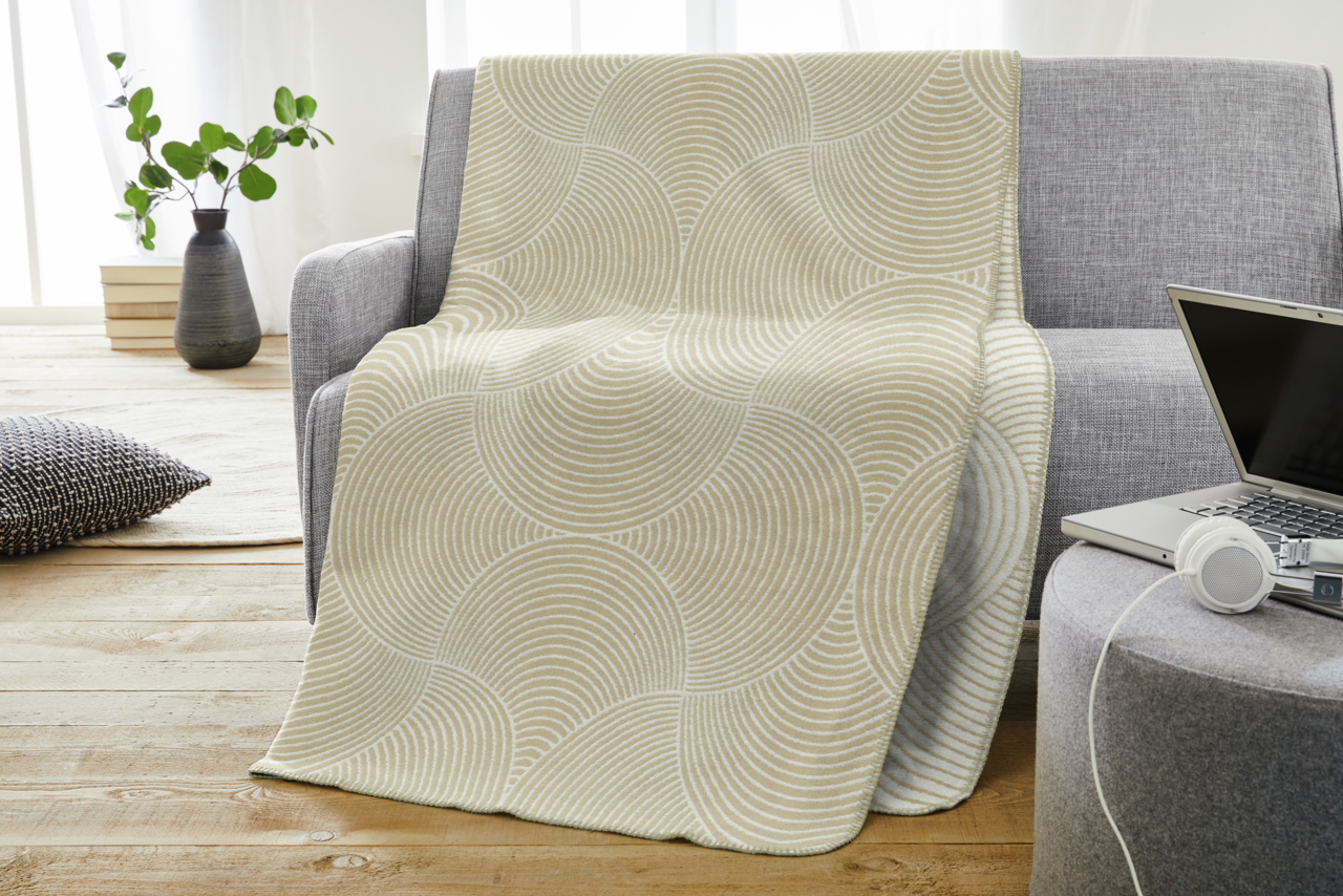 Bugatti Decke BUGATTI Beige Jacquard-Decke mit kreisförmigem Muster, drapiert über einem grauen Sofa in einem modernen Wohnzimmer, seitliche Perspektive.