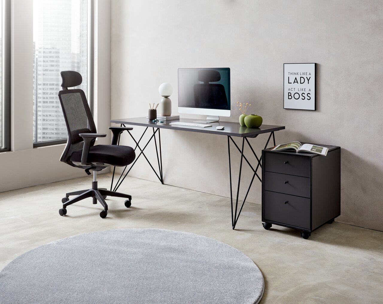 Moderner Schreibtisch mit schwarzem Metallgestell, von der Seite fotografiert, mit Bürostuhl, Computer und Dekorationen in einem hellen Raum.