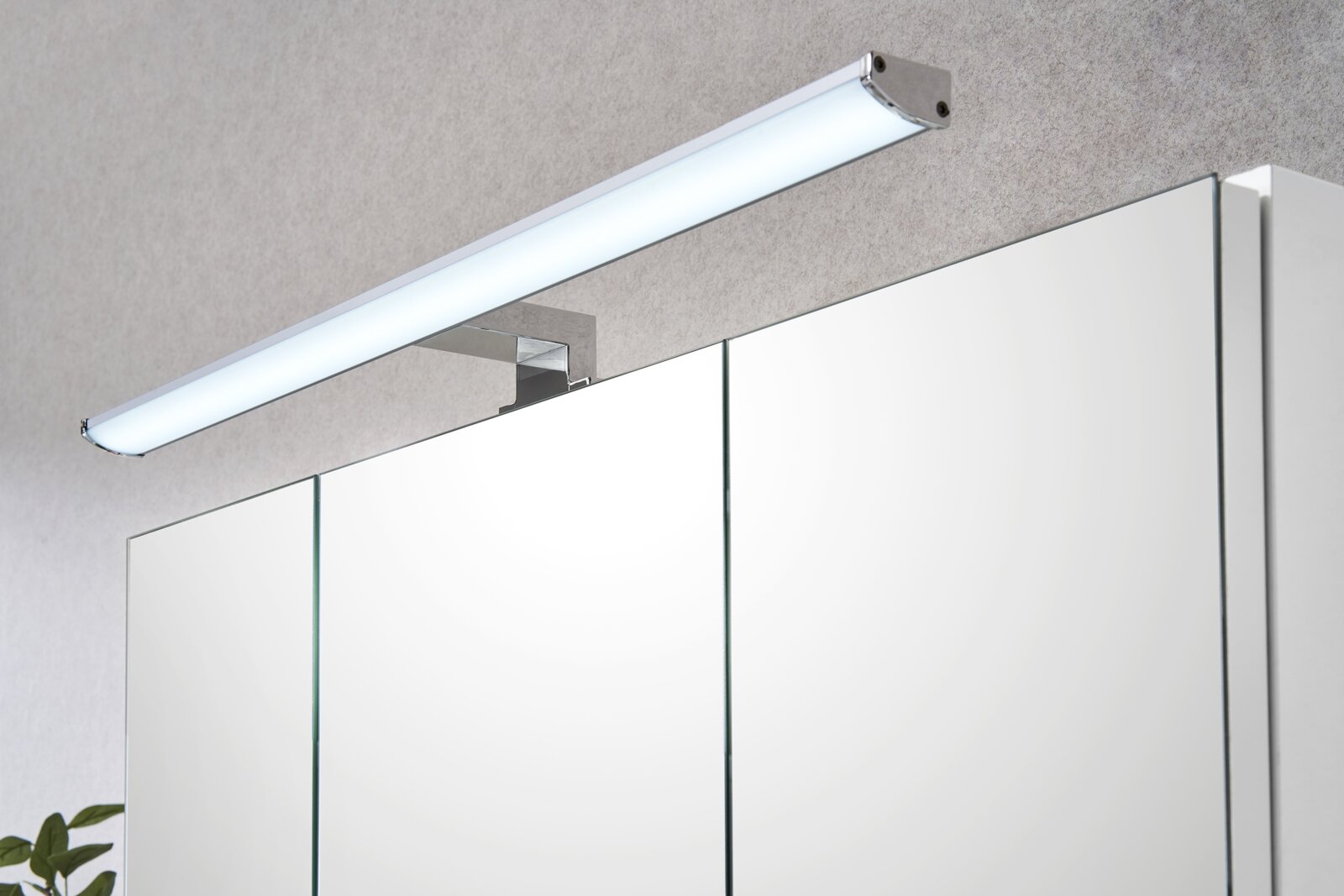 Moderne LED-Spiegelleuchte in Chromoptik über einem Badezimmerspiegelschrank, schräg von vorne oben fotografiert