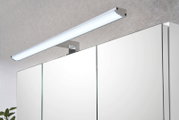 Moderne LED-Spiegelleuchte in Chromoptik über einem Badezimmerspiegelschrank, schräg von vorne oben fotografiert