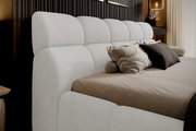 Seitliche Perspektive auf ein elegantes Polsterbett mit einem hohen, gepolsterten Kopfteil in hellem Stoff, dekoriert mit mehreren Kissen in neutralen Tönen.