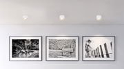 Deckenleuchte aus weißem Metall, von unten betrachtet, beleuchtet eine Wand mit drei schwarz-weißen Fotografien.