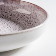 Nahaufnahme einer glasierten Keramikschale mit gesprenkelter Oberfläche in Weiß und Violett, schräg von oben fotografiert (Detailansicht am Rand) auf hellem Hintergrund