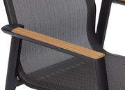 Nahaufnahme eines Stapelstuhls mit schwarzem Rahmen, Holzarmlehnen und gemustertem Stoffbezug, seitliche Perspektive.