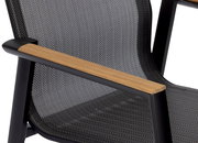 Nahaufnahme eines Stapelstuhls mit schwarzem Rahmen, Holzarmlehnen und gemustertem Stoffbezug, seitliche Perspektive.