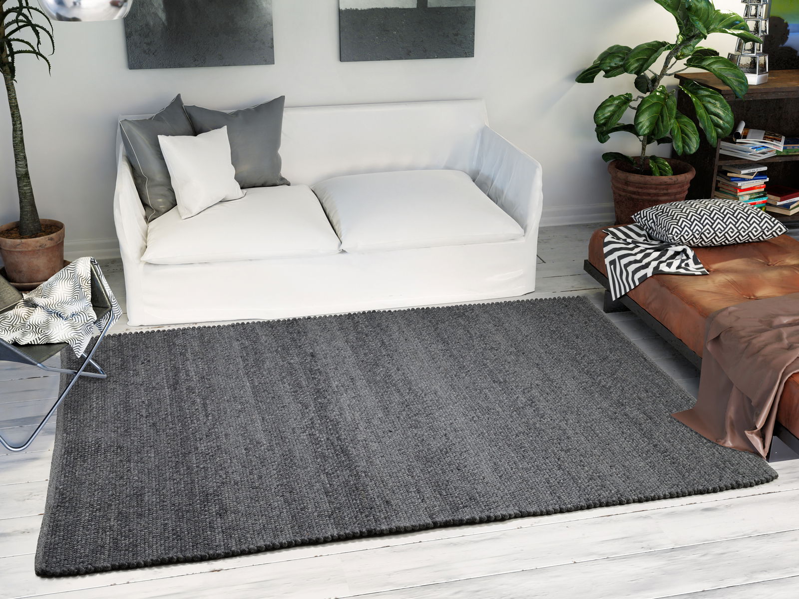 Grauer Handweb Teppich in einem modernen Wohnzimmer, von oben betrachtet, mit weißem Sofa und Pflanzen im Hintergrund.