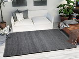 Grauer Handweb Teppich in einem modernen Wohnzimmer, von oben betrachtet, mit weißem Sofa und Pflanzen im Hintergrund.