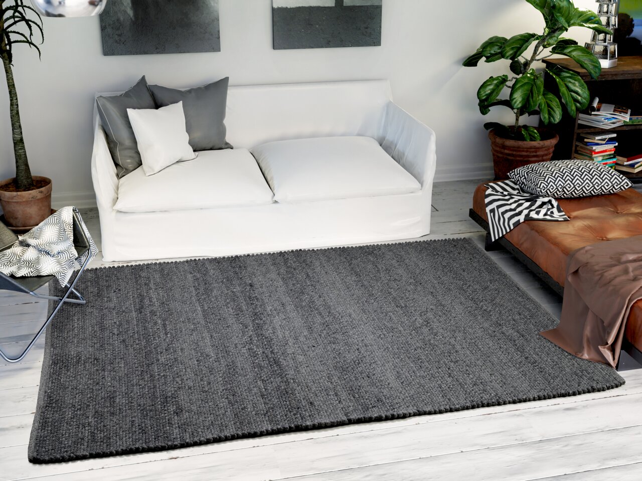 Grauer Handweb Teppich in einem modernen Wohnzimmer, von oben betrachtet, mit weißem Sofa und Pflanzen im Hintergrund.