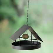 Vogelfutterstation Solto, H 22, aus schwarzem Metall, hängend an einer Kette, mit einem Meisenknödel im Inneren, seitliche Perspektive.