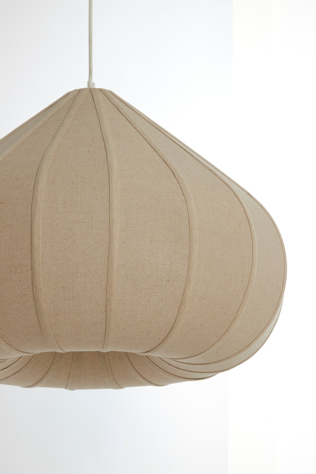 Close-up van een beige hanglamp met een stoffen oppervlak en een gebogen vormgeving, gezien vanaf de zijkant.