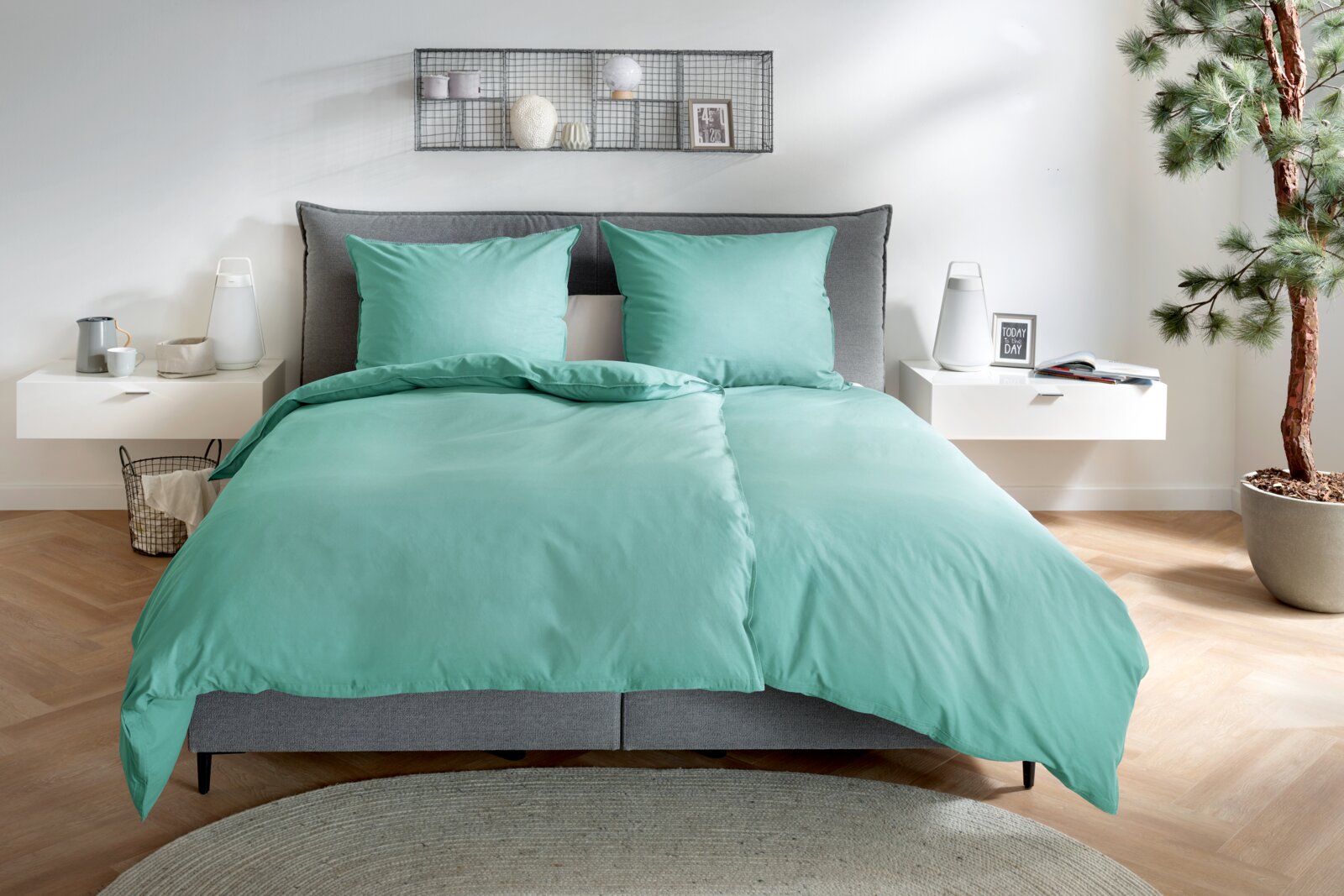 Primera Renforce Bettwäsche 135/200cm Mintgrüne Bettwäsche mit zwei passenden Kissenbezügen auf einem grauen Polsterbett im modern eingerichteten Schlafzimmer, frontal aus leicht erhöhter Perspektive fotografiert