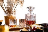 Whisky-Set Noblesse mit einer Karaffe und zwei Gläsern, gefüllt mit Whisky, auf einem Tisch mit dekorativen Elementen, seitliche Perspektive