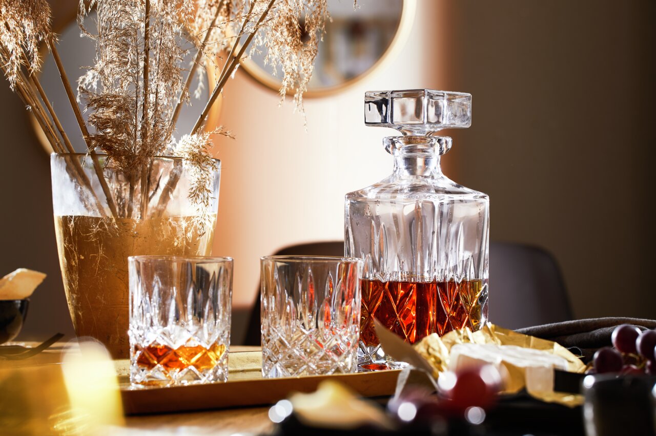 Whisky-Set Noblesse mit einer Karaffe und zwei Gläsern, gefüllt mit Whisky, auf einem Tisch mit dekorativen Elementen, seitliche Perspektive