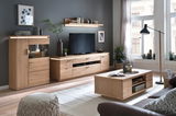 Wohnzimmeransicht mit moderner Wohnkombination aus hellem Holz, bestehend aus TV-Schrank, Vitrine und Couchtisch, mit Dekorationen und Pflanzen, seitliche Perspektive.