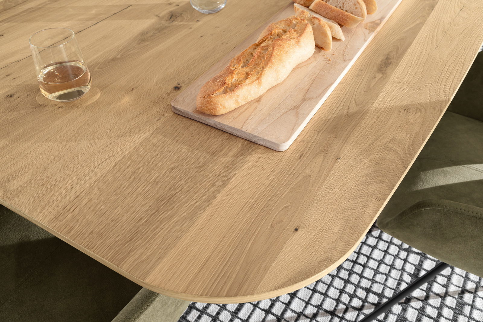 Nahaufnahme eines Venjakob Esstisches ET613 aus Holz mit abgerundeten Ecken, darauf ein Glas und ein Baguette auf einem Schneidebrett. Perspektive von oben.