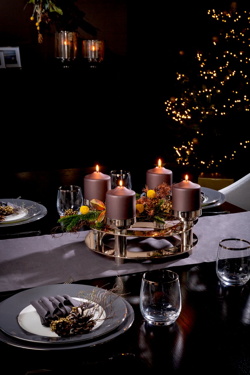 Elegante vierarmige kandelaar met paarse kaarsen en feestelijke versiering op een gedekte tafel, gezien vanuit de zijkant.