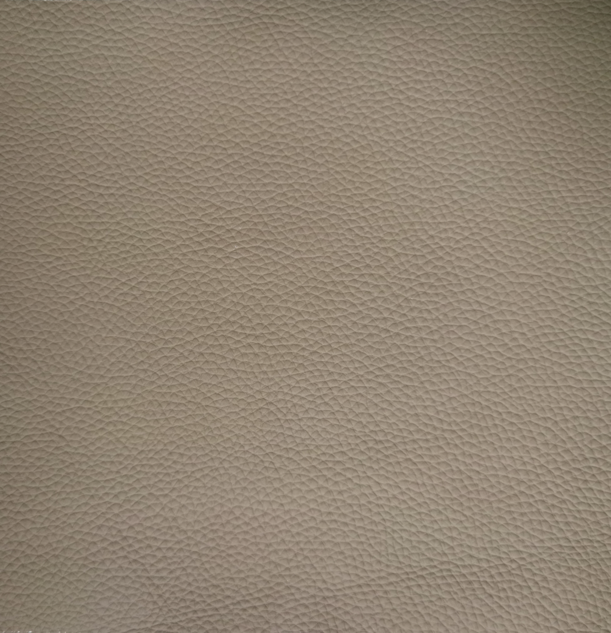 Nahaufnahme einer beige strukturierten Lederoberfläche, die für einen Armlehnstuhl verwendet wird.