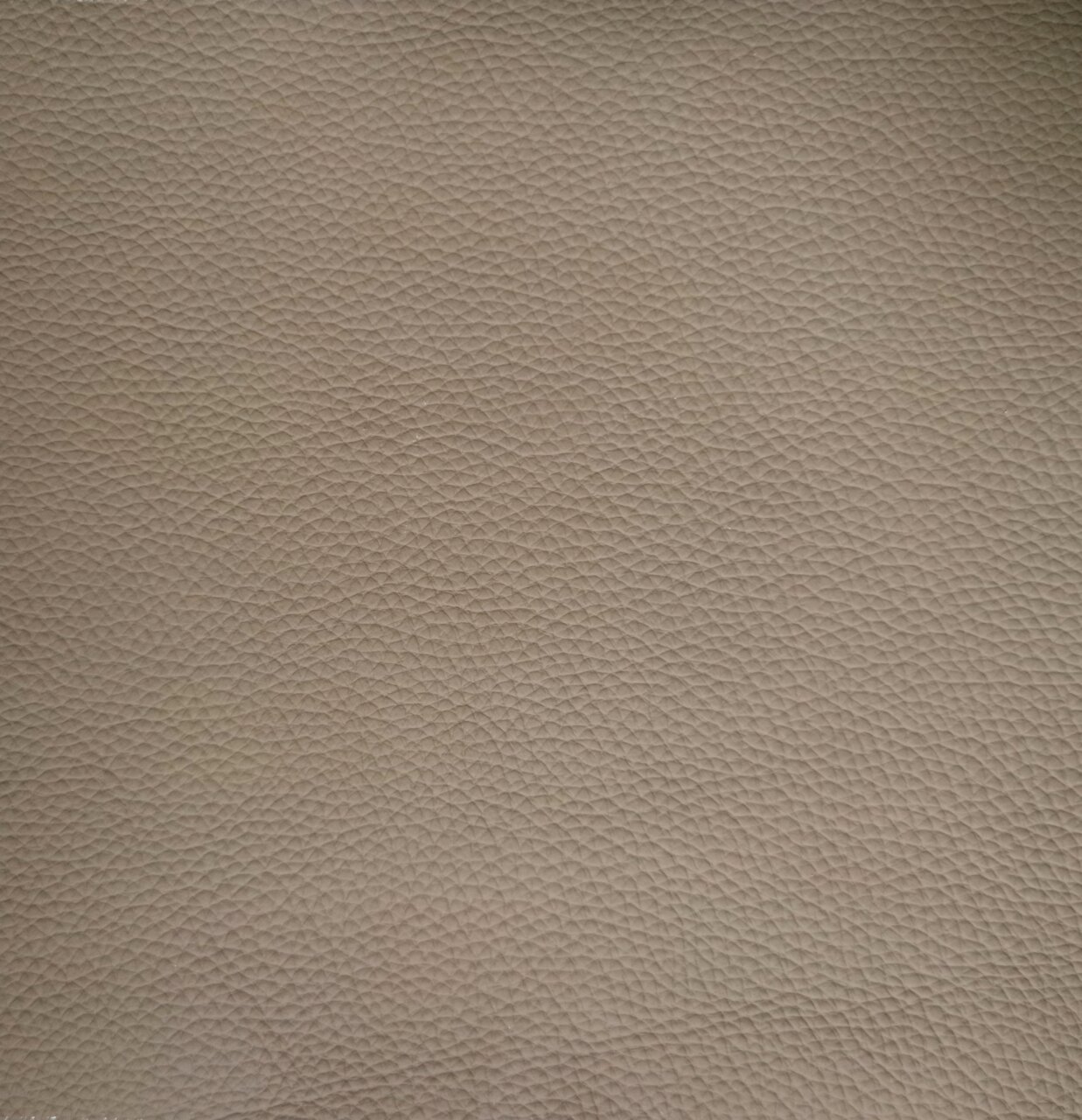 Nahaufnahme einer beige strukturierten Lederoberfläche, die für einen Armlehnstuhl verwendet wird.