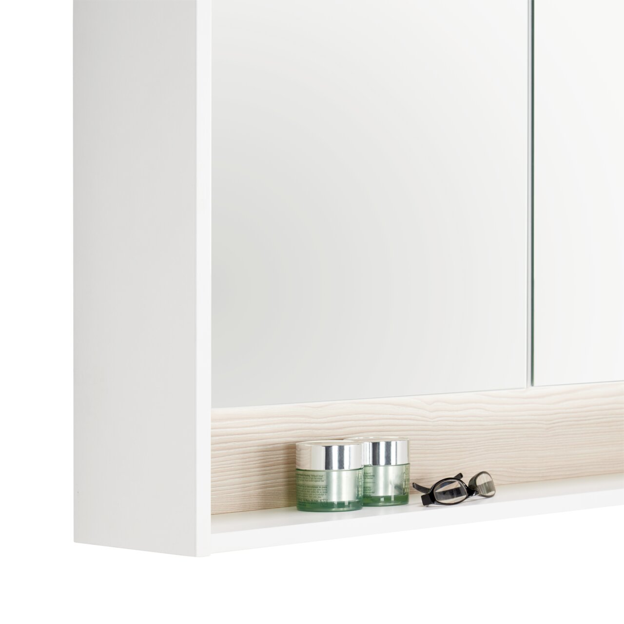 Nahaufnahme eines weißen Spiegelschranks mit zwei Glastiegeln und einer Brille auf einem Regalbrett, seitliche Perspektive
