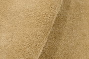 Nahaufnahme eines beigen Uni-Teppichs mit weicher Textur, von der Seite betrachtet.