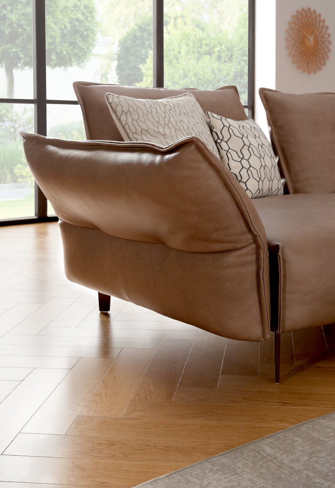 Nahaufnahme einer eleganten, braunen Polsterrundecke mit modernen Kissen, seitliche Perspektive.