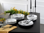 Weißes Porzellan-Geschirrset mit schwarzem floralen Dekor (Teller und Schalen) auf schwarzem Tisch, dekoriert mit gelben Blumen und schwarzem Besteck, Ansicht schräg von vorne leicht von oben.