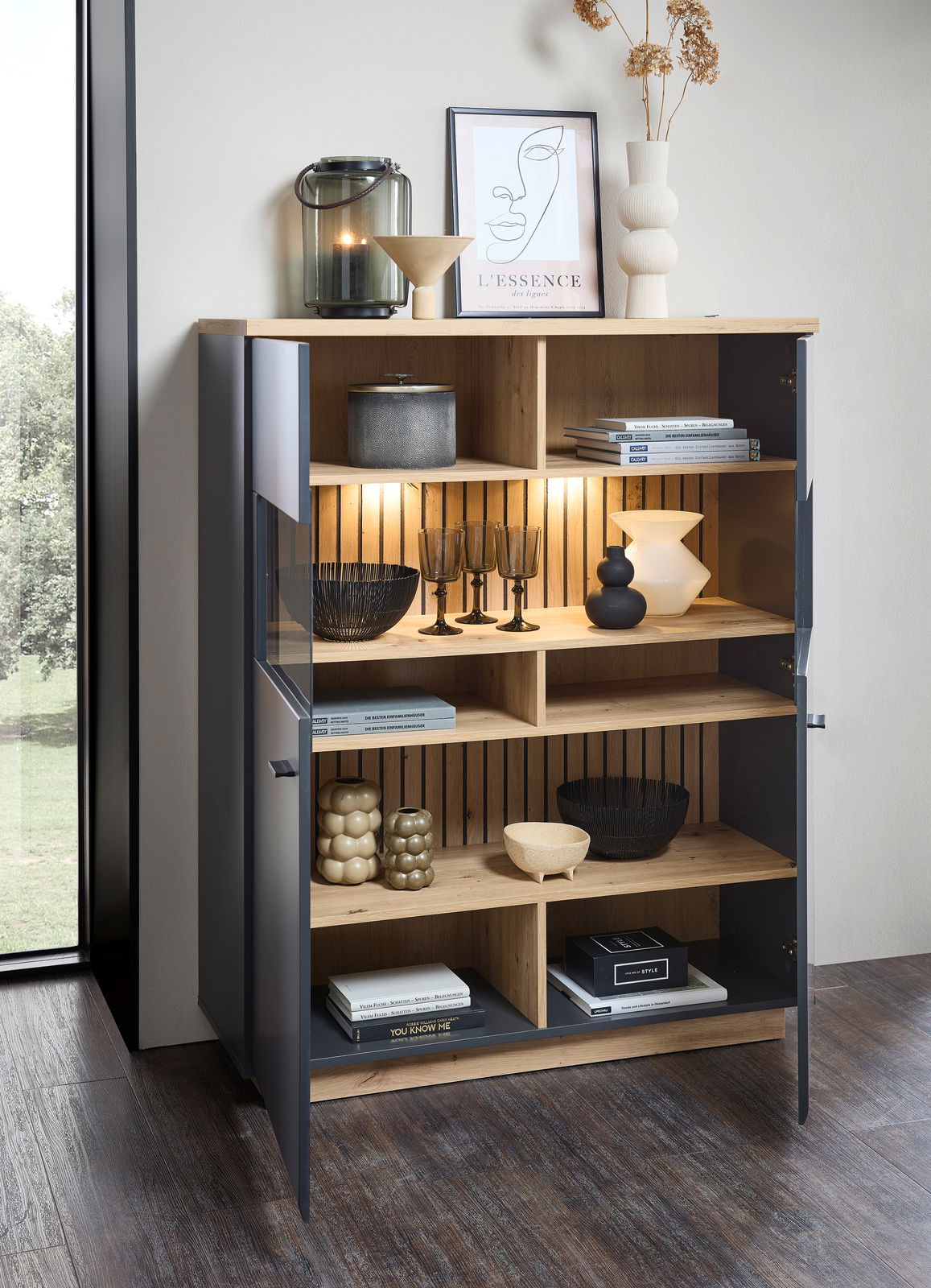 Modernes Highboard mit offenen und geschlossenen Fächern, dekoriert mit Büchern, Vasen und Gläsern, aus einer schrägen Perspektive fotografiert.